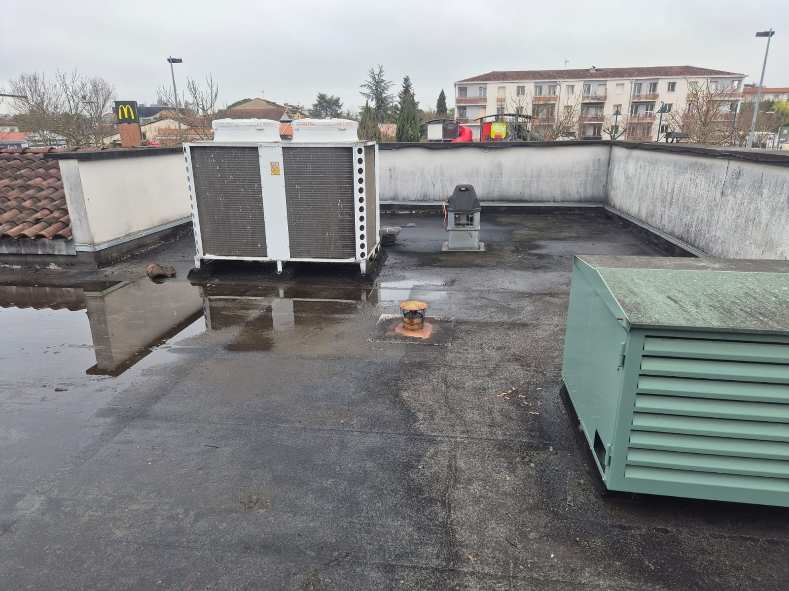 Toiture-terrasse avec équipements CVC et eau stagnante Unité de climatisation et évents sur une toiture-terrasse mouillée avec vue sur des bâtiments résidentiels.